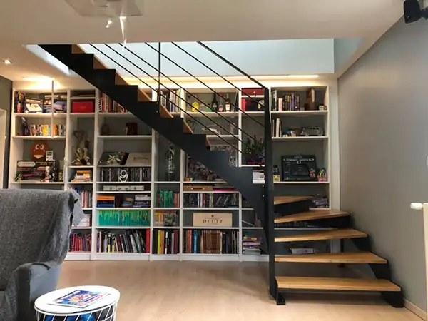 Escalier droit sur mesure en métal noir avec marches en bois, intégré dans un salon avec bibliothèque
