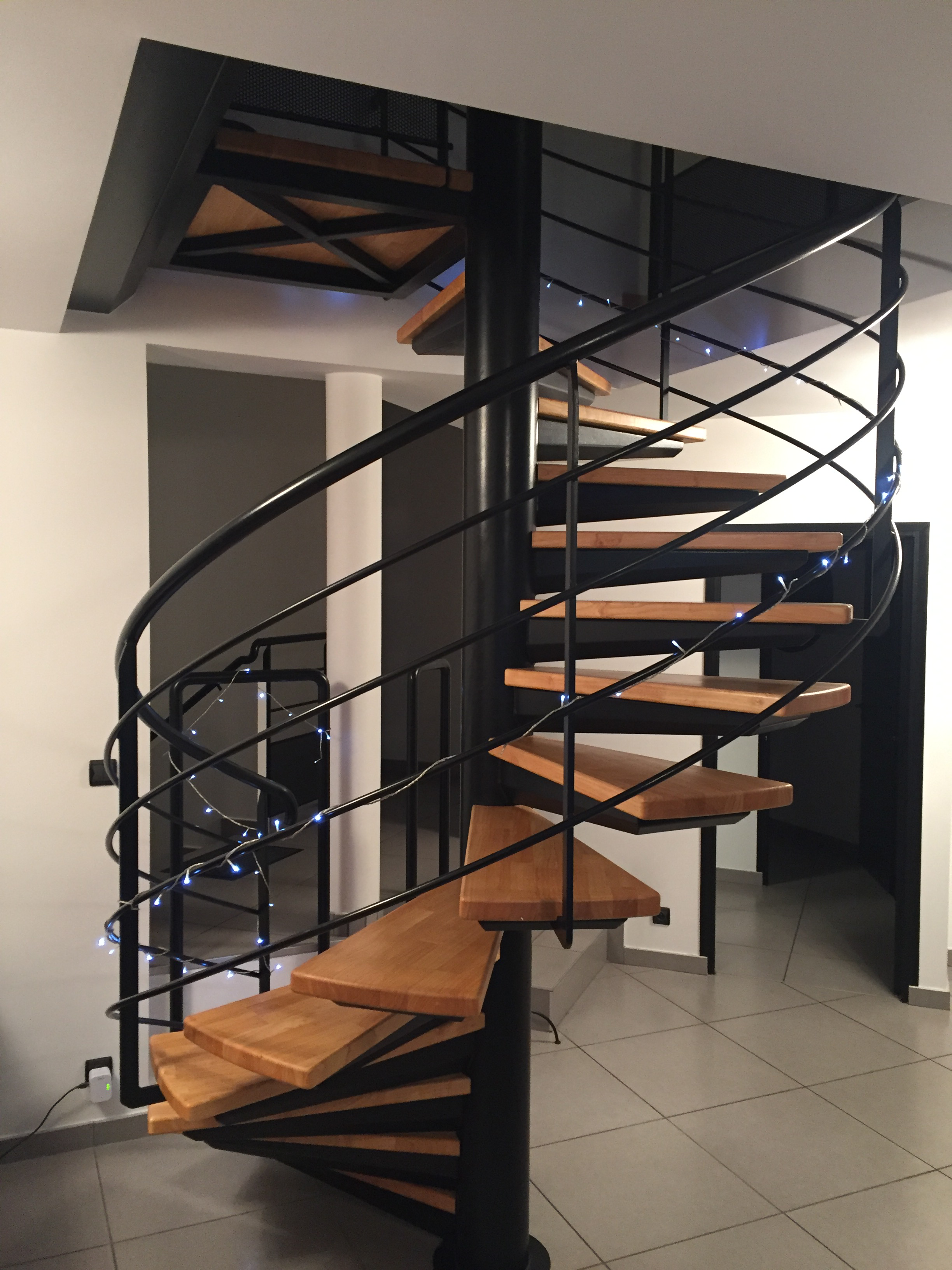 Escalier colimaçon en métal noir avec marches en bois et garde-corps courbe