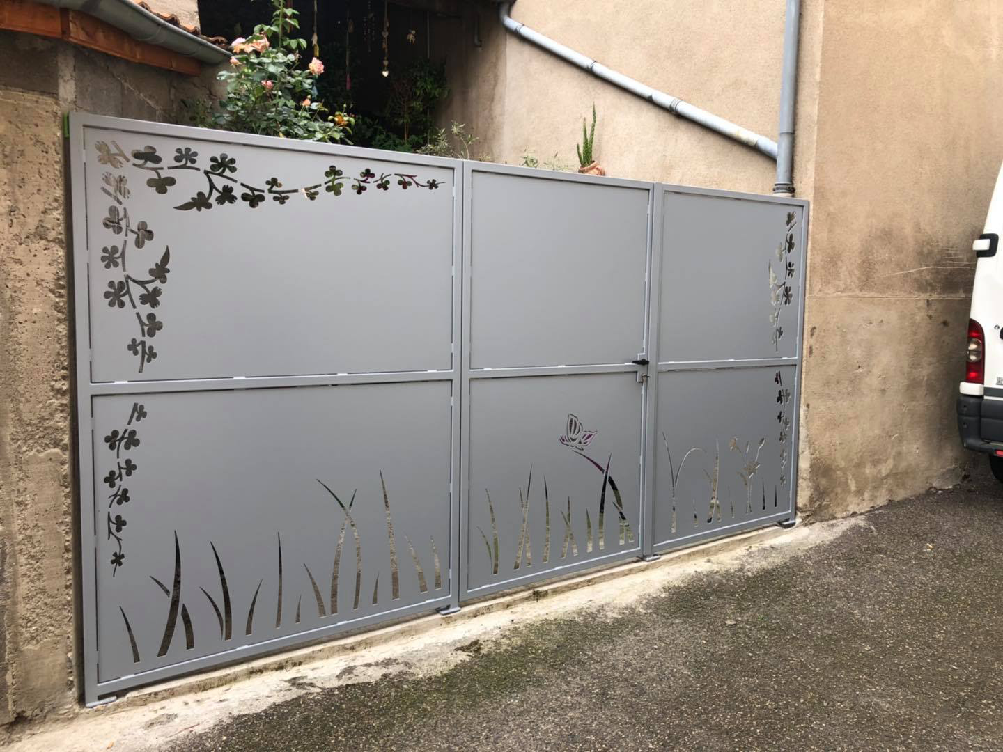 Portail battant en métal gris avec motif végétal découpé