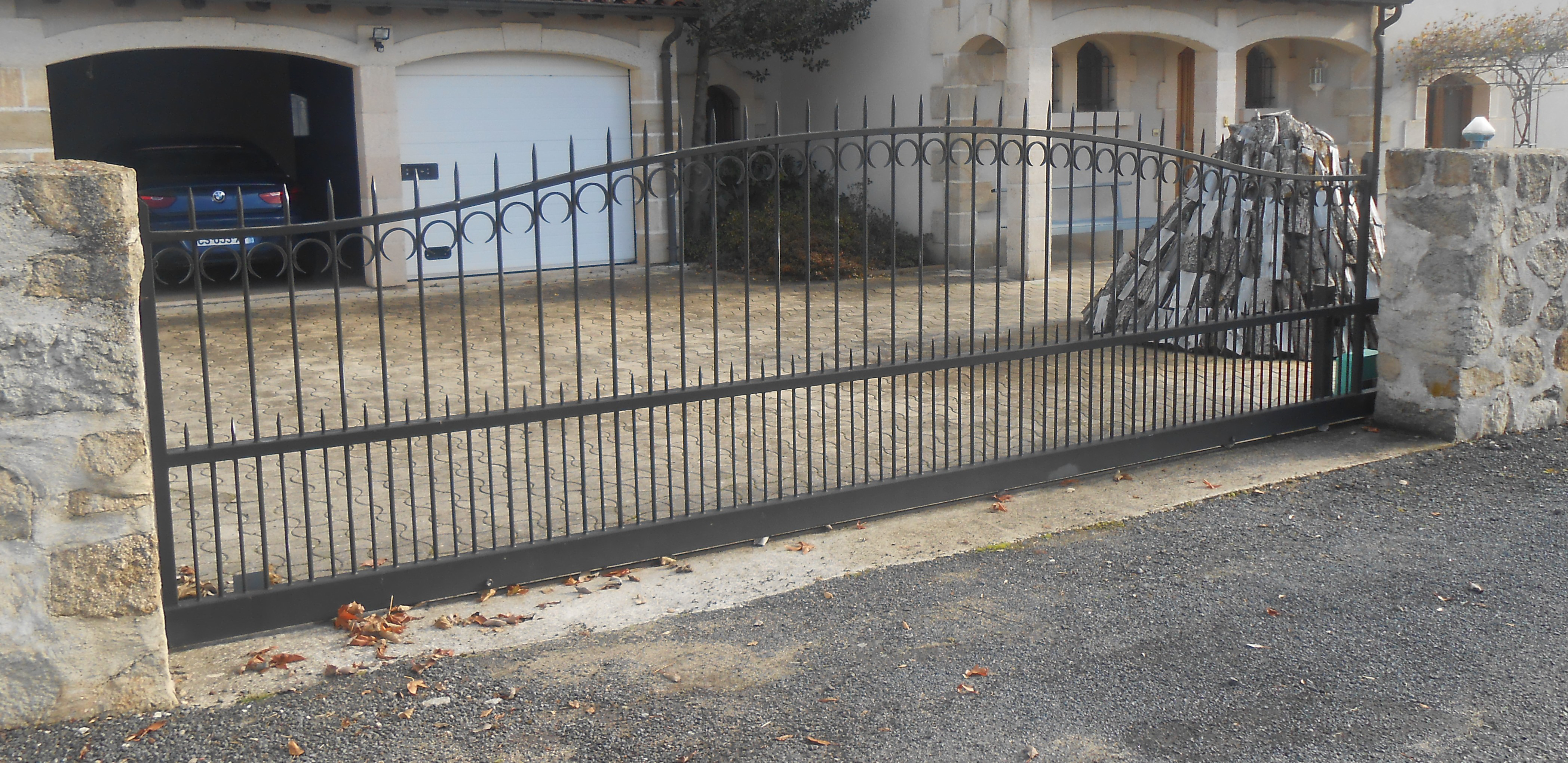 Portail coulissant en ferronnerie noire avec barreaux verticaux, pointes et volutes, installé entre deux piliers en pierre