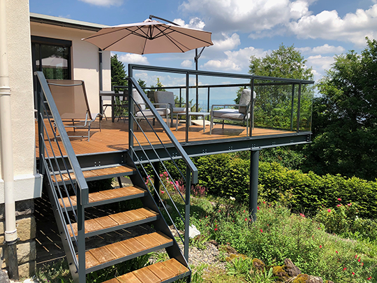 Terrasse surélevée sur mesure avec structure métallique, escalier extérieur en bois et garde-corps en métal et verre