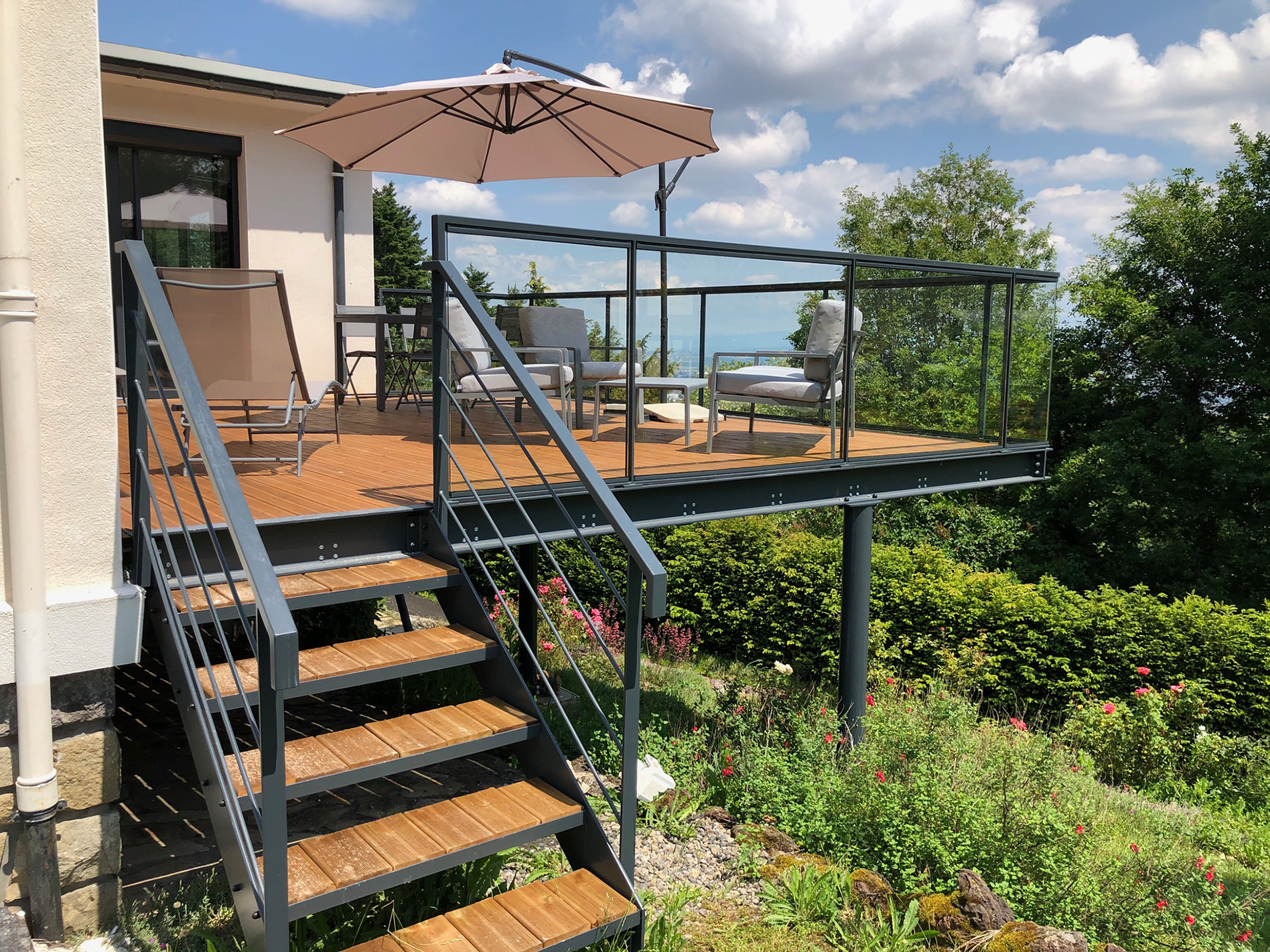 Terrasse surélevée sur mesure avec structure métallique, escalier extérieur en bois et garde-corps en métal et verre