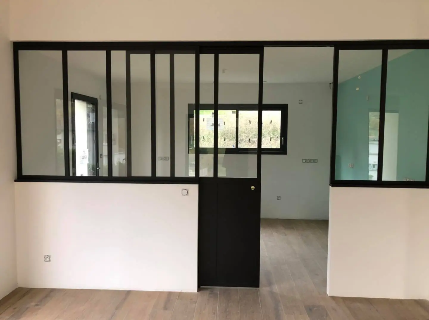 Grande verrière intérieure noire avec porte coulissante, séparant deux pièces